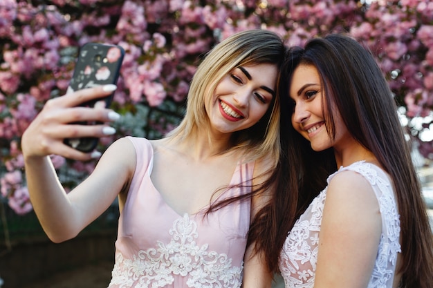 Due ragazze prendono selfie prima di un bellissimo albero di sakura nel parco