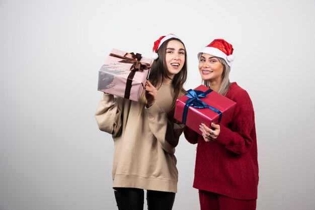 Due ragazze sorridenti in cappello della Santa che tengono i regali di Natale festivi.