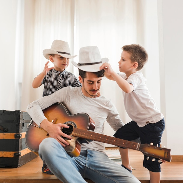 Due ragazzi che giocano con il loro padre tenendo la chitarra