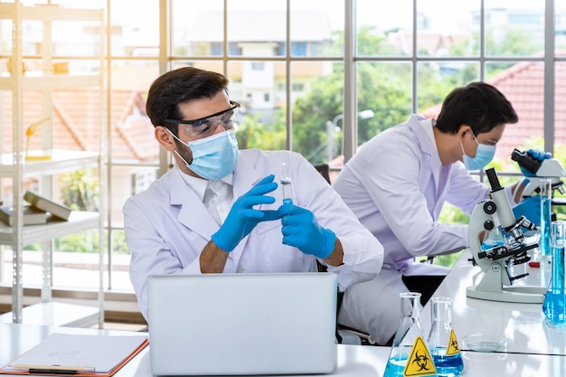 Due ricercatori maschi asiatici e arabi che lavorano in laboratorio conducendo lo studio di sostanze a rischio biologico con attrezzature scientifiche e microscopio