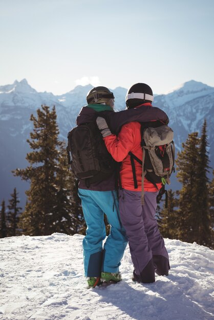 Due sciatori che stanno insieme con il braccio intorno sulla montagna innevata
