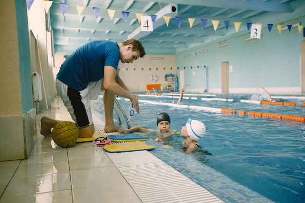 Due scolarette giocatori di pallanuoto che ascoltano l'insegnante a bordo piscina. Divertiti, gioca e tuffati in una piscina blu