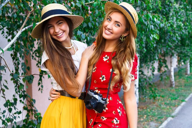 Due sorelle abbastanza giovani felici, abbracci sorridenti ridendo e divertendosi insieme, portando vestiti e cappelli femminili vintage retrò alla moda. All'aperto.