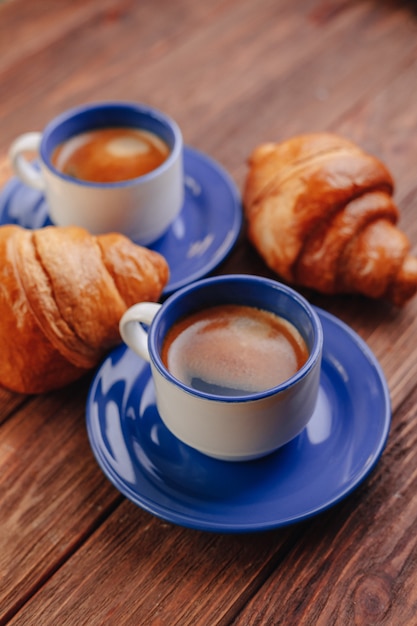 Due tazze di caffè e cornetti su uno sfondo di legno, buona luce, atmosfera mattutina