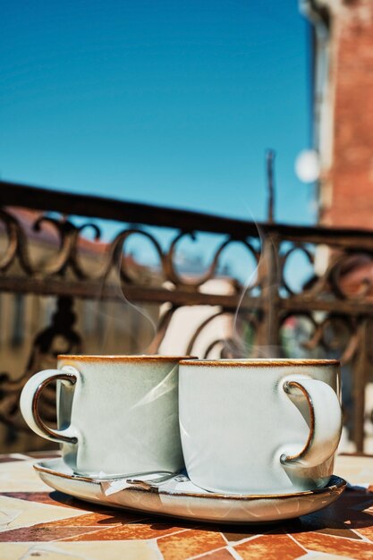 Due tazze di tè caldo su un tavolo vintage su una vecchia terrazza il vapore sale su tazze di bevanda calda Idea per il tè pomeridiano banner sullo sfondo della città vecchia chiara giornata di sole cornice verticale messa a fuoco selettiva