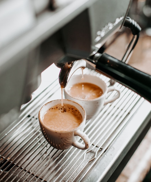 Due tazzine da caffè sotto il motore del caffè