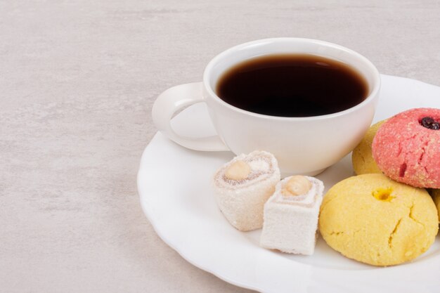 Due tipi di biscotti, delizie e una tazza di tè sul piatto bianco.