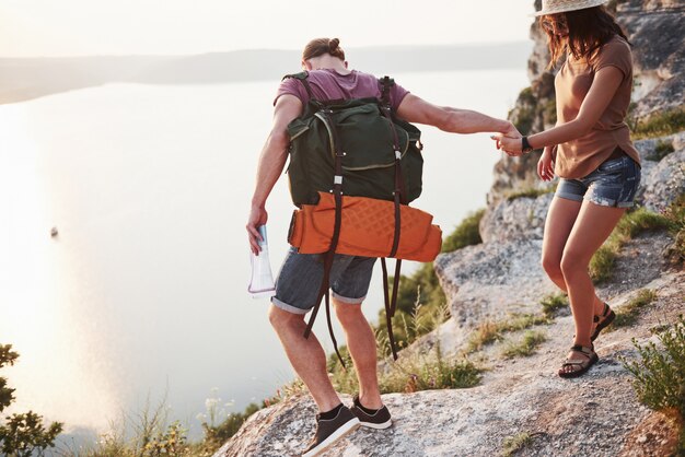 Due uomini e due donne turistiche con zaini si arrampicano sulla cima della montagna e si godono l'alba.