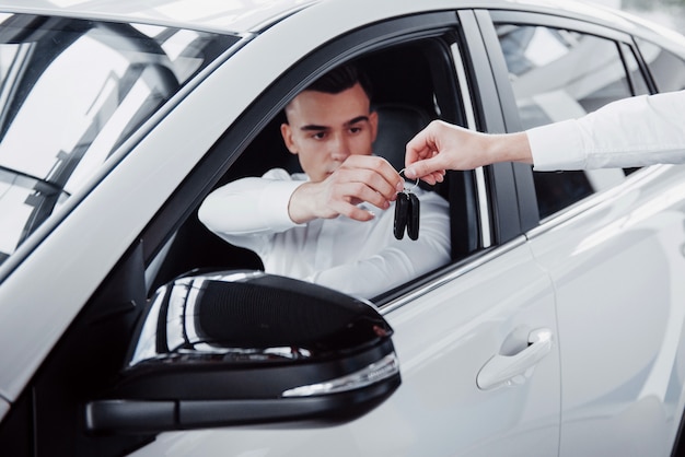 Due uomini stanno nello showroom contro le macchine. Primo piano di un responsabile vendite in una tuta che vende un'auto a un cliente. Il venditore fornisce la chiave al cliente.