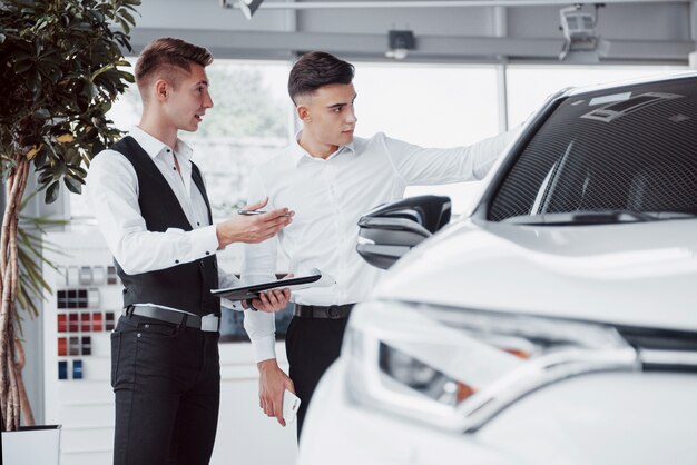 Due uomini stanno nello showroom contro le macchine. Primo piano di un responsabile vendite in una tuta che vende un'auto a un cliente. Il venditore fornisce la chiave al cliente.