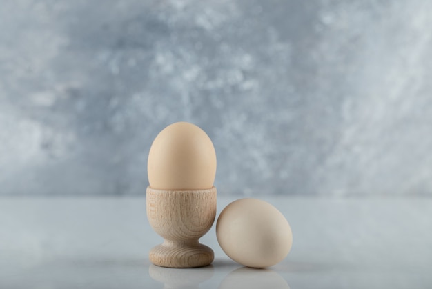 Due uova fresche in portauovo e macinate su sfondo bianco.