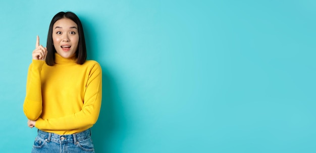 Eccitata donna asiatica con capelli scuri corti che lancia un'idea alzando il dito nel gesto eureka e smili