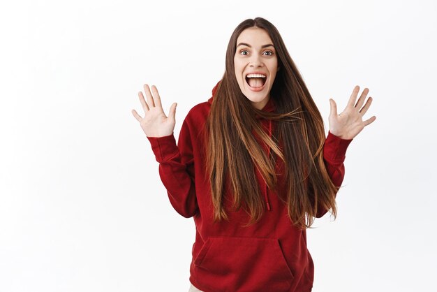 Eccitata ragazza divertente urlare dalla gioia lunghi capelli naturali che volano in aria la signora corre le mani in alto e gridando dallo stupore e dall'eccitazione controllando il fantastico affare promozionale su sfondo bianco