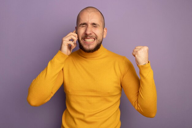 Eccitato con gli occhi chiusi giovane bel ragazzo parla al telefono e mostrando sì gesto isolato sulla parete viola