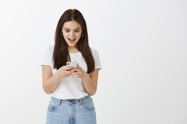 Eccitato giovane donna in posa con il suo telefono contro il muro bianco