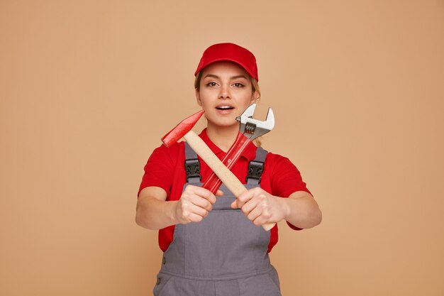 Eccitato giovane operaio edile femminile che indossa berretto e uniforme allungando la chiave e il martello verso la telecamera senza fare alcun gesto