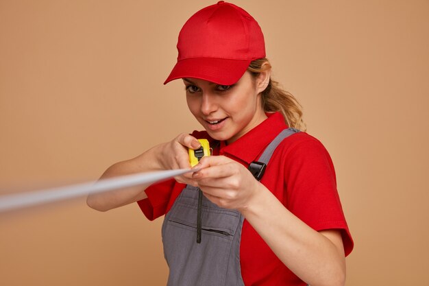 Eccitato giovane operaio edile femminile che indossa berretto e uniforme che allunga il metro a nastro verso la telecamera