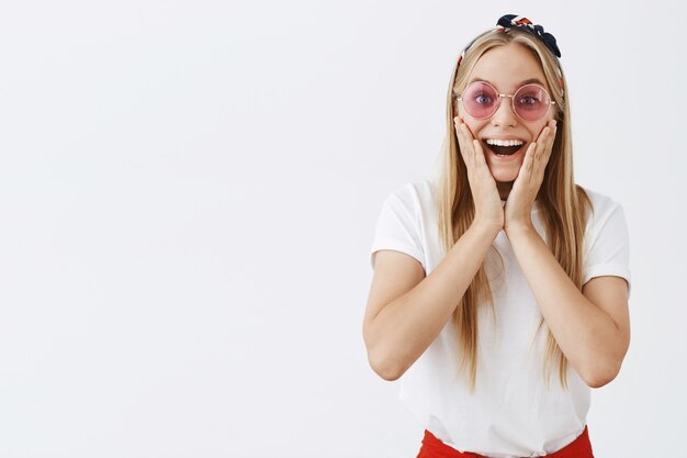 Eccitato giovane ragazza bionda sorridente in posa contro il muro bianco