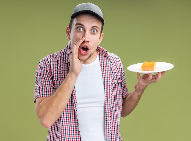 Eccitato giovane ragazzo pulitore che indossa il cappuccio tenendo la spugna sulla piastra chiamando qualcuno isolato sulla parete verde oliva