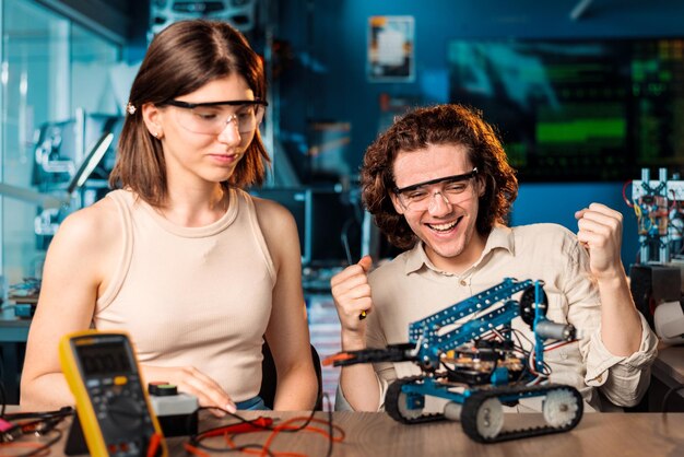Eccitato giovane uomo e donna in occhiali protettivi che fanno esperimenti di robotica in un laboratorio