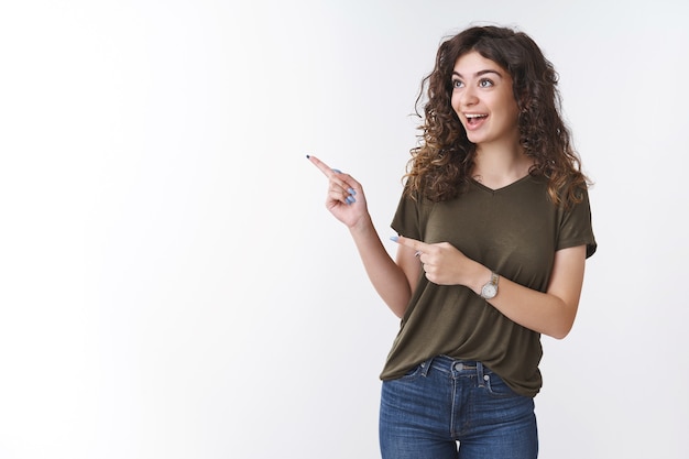 Eccitato in uscita allegro caucasica ragazza dai capelli ricci che indossa oliva t-shirt sorridente divertito puntamento guardando affascinato angolo sinistro in piedi entusiasta interessato vuole acquistare un abito fantastico per il ballo di fine anno