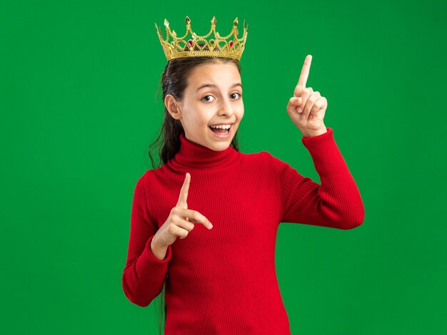 Eccitato ragazza adolescente che indossa la corona rivolta verso l'alto isolata sulla parete verde con spazio di copia
