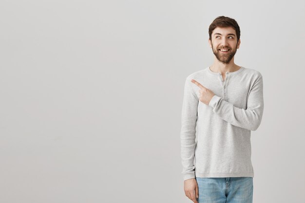 Eccitato ragazzo barbuto sorridente che punta il dito nell'angolo superiore sinistro