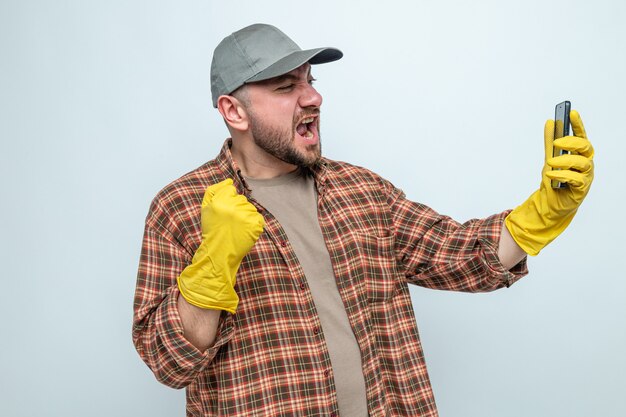 Eccitato uomo delle pulizie slavo con guanti di gomma che tiene il pugno e guarda il telefono