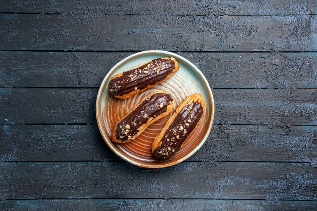 Eclairs al cioccolato vista in lontananza sulla piastra ovale sul tavolo di legno scuro