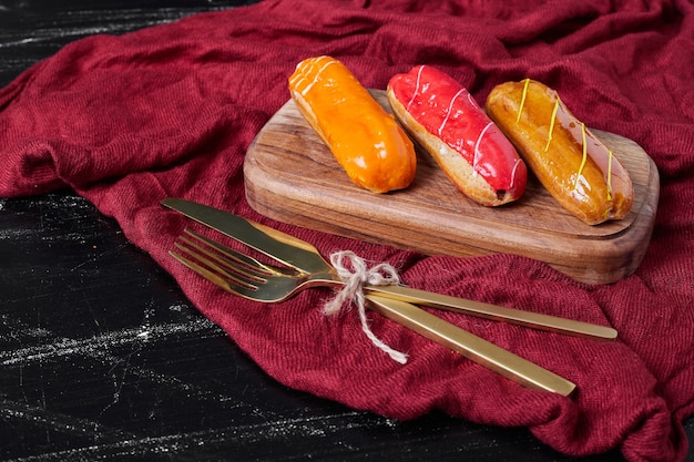 Eclairs con sciroppi colorati su un piatto di legno con posate.