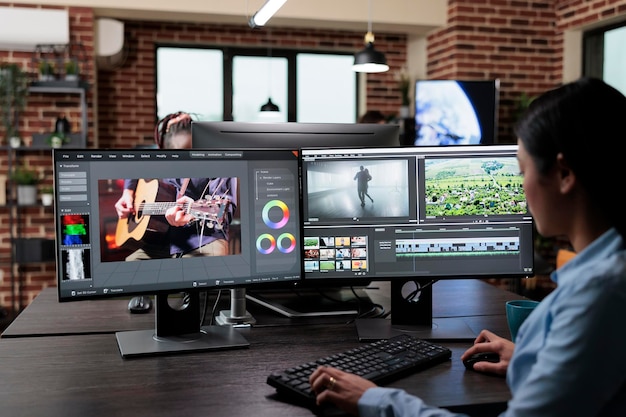 Editor di filmati professionali per aziende creative seduto su una workstation multi monitor durante la modifica dei fotogrammi del film. Videografo esperto che migliora la qualità video utilizzando software specializzati.