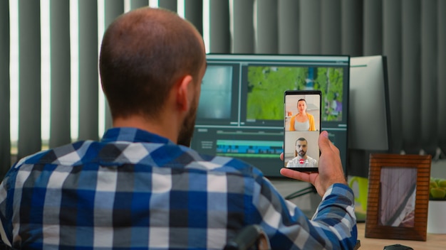 Editor video freelance con disabilità in sedia a rotelle che ha videochiamata durante la modifica della postproduzione di un progetto che crea contenuti nel moderno ufficio dell'azienda. Videografo che lavora da studio fotografico