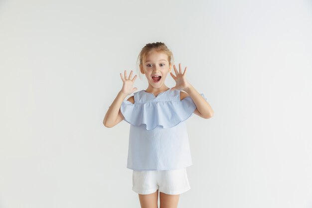 Elegante bambina sorridente in posa in abiti casual isolati su sfondo bianco studio. Modello femminile biondo caucasico. Emozioni umane, espressione facciale, infanzia, vendite. Scioccato, stupito.