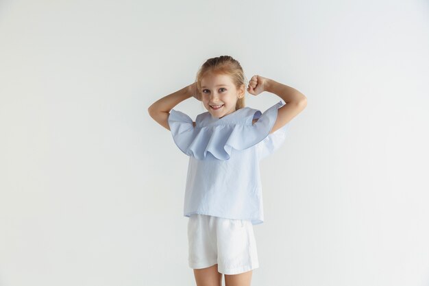 Elegante bambina sorridente in posa in abiti casual isolati su spazio bianco. Modello femminile biondo caucasico. Emozioni umane, espressione facciale, infanzia