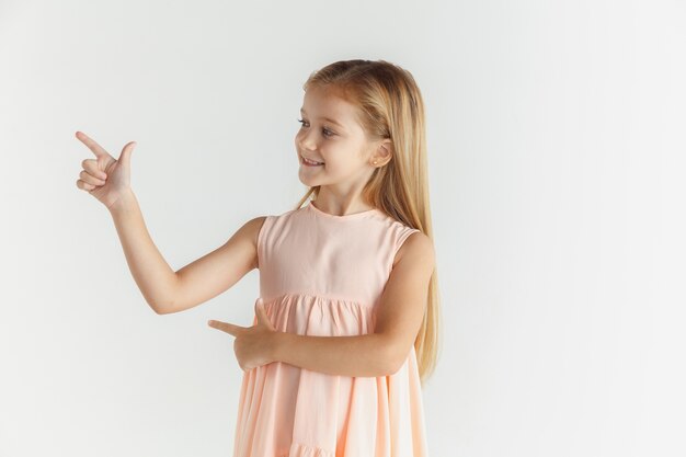 Elegante bambina sorridente in posa in abito isolato su sfondo bianco studio. Modello femminile biondo caucasico. Emozioni umane, espressione facciale, infanzia. Puntando sulla barra spaziatrice vuota.