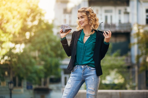 Elegante bella donna in jeans e giacca che cammina in strada con borsetta, stile elegante, tendenze della moda primaverile