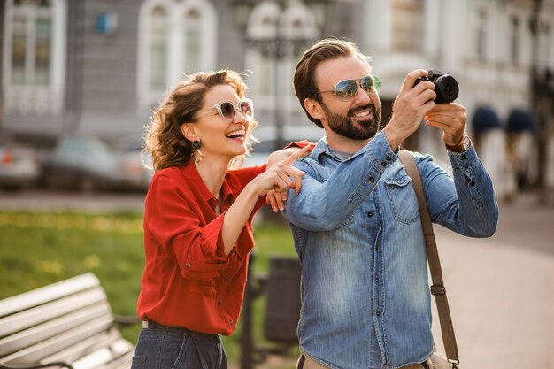 Elegante coppia innamorata che cammina abbracciata in strada durante un viaggio romantico e scatta foto