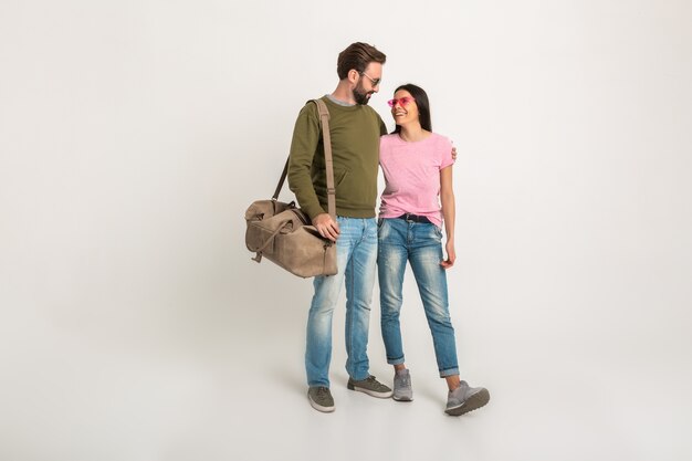 Elegante coppia isolata, bella donna sorridente in maglietta rosa e uomo in felpa che tiene borsa da viaggio, vestito in jeans, indossando occhiali da sole, divertirsi insieme