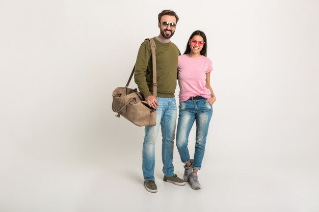 Elegante coppia isolata, bella donna sorridente in maglietta rosa e uomo in felpa che tiene borsa da viaggio, vestito in jeans, indossando occhiali da sole, divertirsi insieme