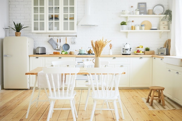 Elegante cucina scandinava interni: sedie e tavolo in primo piano, frigorifero, lungo bancone in legno con macchine, utensili sugli scaffali. Interni, design, idee, concetto di casa e intimità