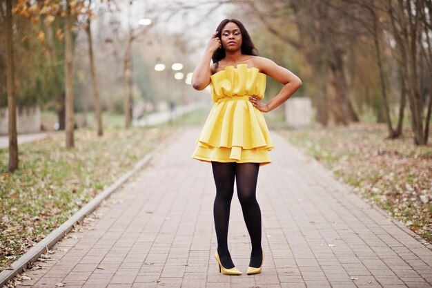 Elegante donna afroamericana in abito giallo in posa contro il parco autunnale