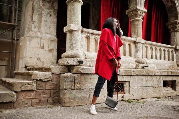 Elegante donna afroamericana in cappotto rosso posata contro vecchie colonne