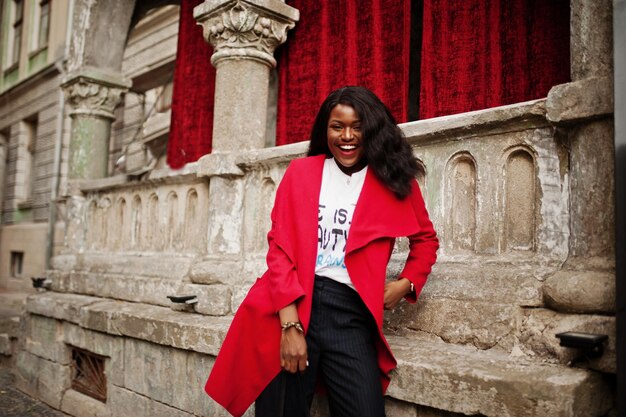 Elegante donna afroamericana in cappotto rosso posata contro vecchie colonne