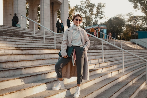 Elegante donna alla moda che cammina per strada con un cappotto in stile elegante