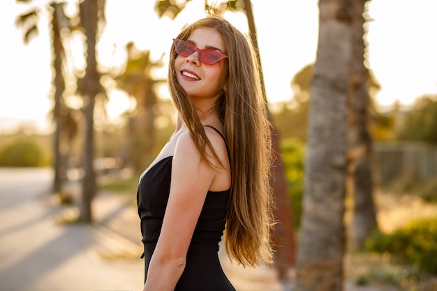 Elegante donna alla moda in posa vicino a palme al tramonto