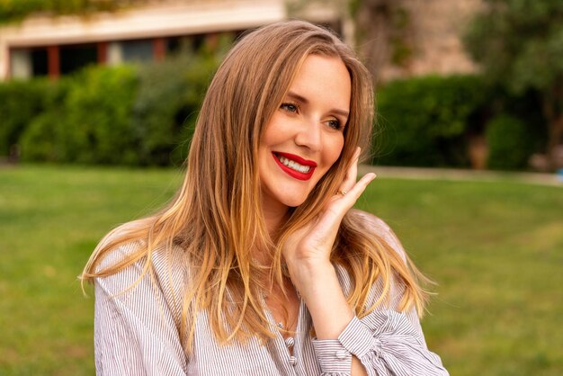 Elegante donna bionda blogger in posa vicino alla vecchia casa di un hotel di lusso, con indosso pantaloncini bianchi e camicetta, stile elegante.