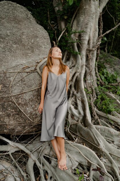 Elegante donna bruna in abito grigio seta in posa sulle rocce