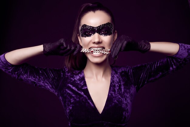 Elegante donna bruna in un bellissimo vestito viola, maschera di paillettes e guanti neri