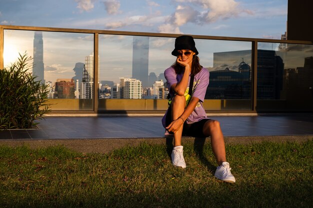 Elegante donna caucasica in panama alla moda e borsa al neon in vita sul tetto a Bangkok