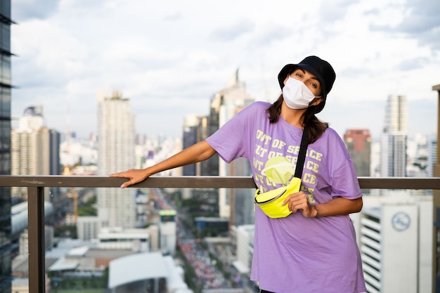 Elegante donna caucasica in panama alla moda e borsa al neon in vita sul tetto a Bangkok